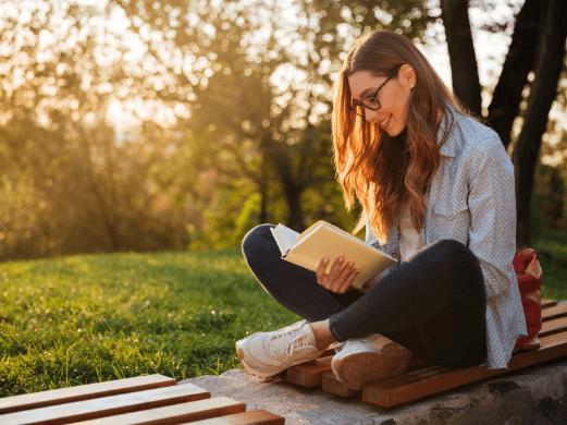 Eine Frau sitzt in der Natur und liest ein Buch