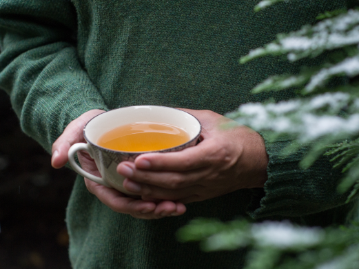 a person in green sweater is holding a cup of tea
