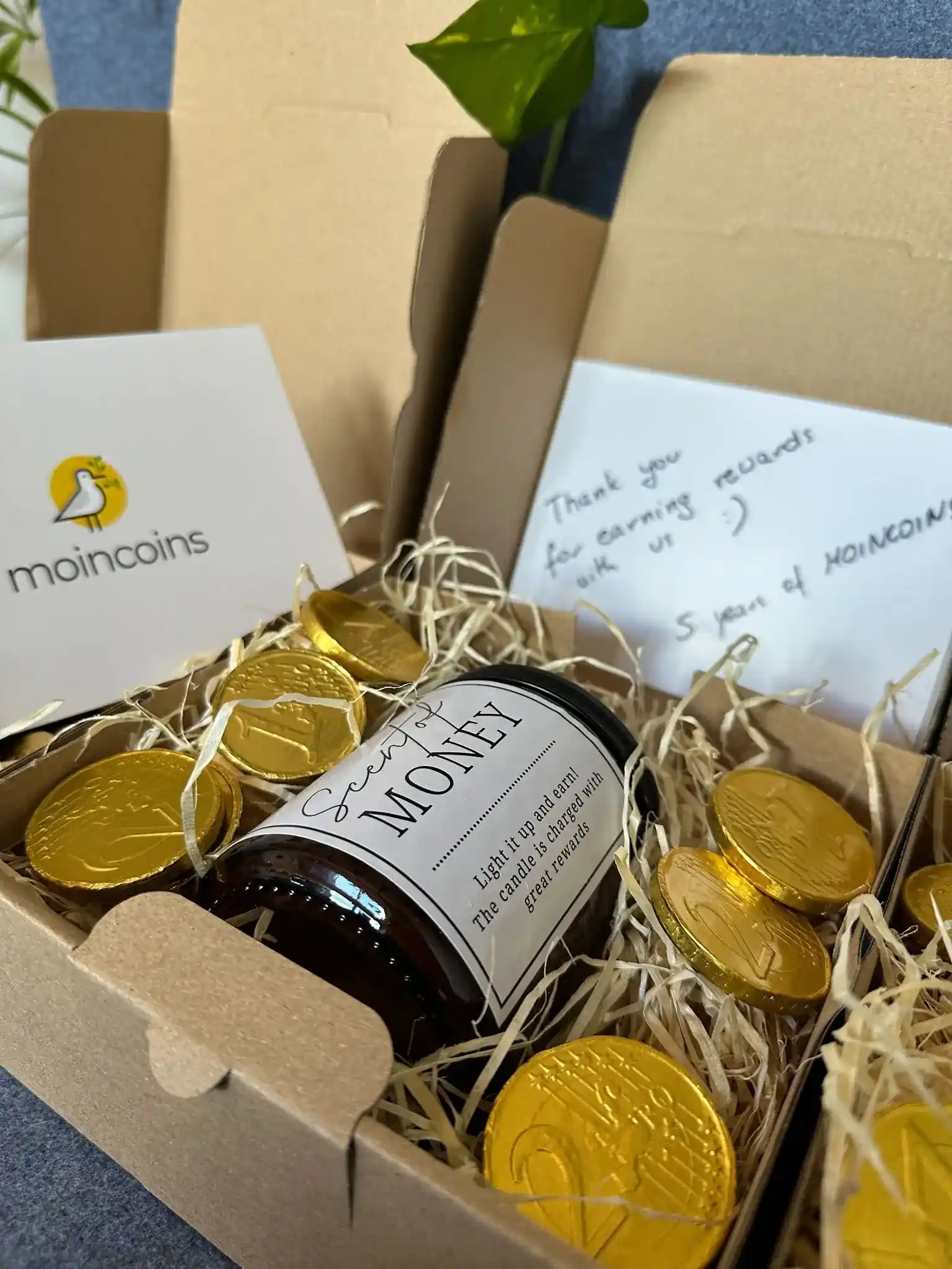 Moincoins 5th anniversary gift boxes with candles, chocolate coins, and thank-you letters arranged together.
